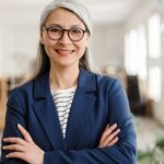 the smiling asian woman standing with crossing arms in the office